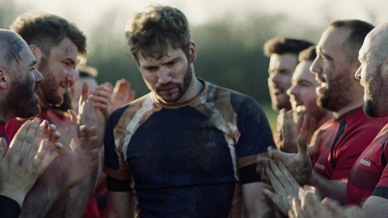 Head and shoulders shot of a group of men wearing rugby jerseys huddled closely together on a field