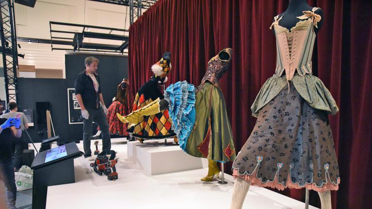 A man on a stage looking at a line-up of mannequins wearing different costumes from the film Moulin Rouge!