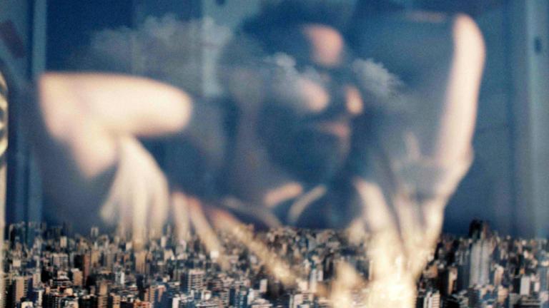 Reflection in a window of a man with his arms raised over his head. Through the window you can see a city skyline.