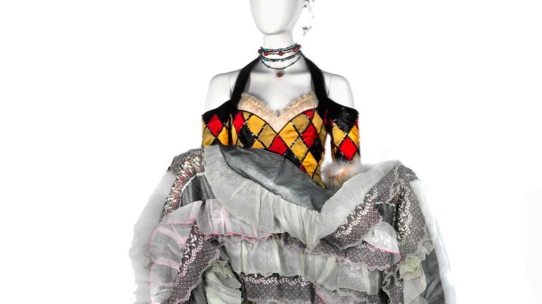 Costume on a mannequin featuring off-the-shoulder sleeves and a bodice and a full skirt that has a harlequin design on it. The skirt has been turned up to show the layers of lace petticoats underneath the main fabric of the skirt. The costume was worn by a dancer in the film Moulin Rouge!