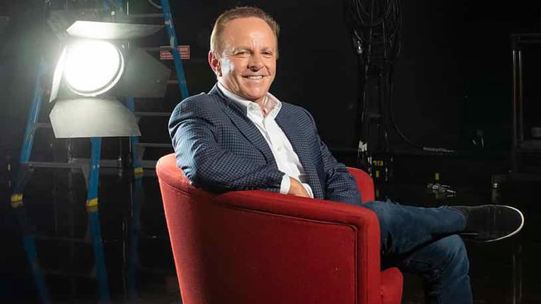 Television executive Brian Walsh seated in a red armchair smiling at camera.