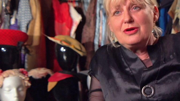 Costume designer Marion Boyce pictured sitting down surrounded by dresses and costume accessories.
