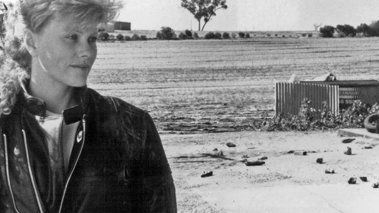 Actor Deborra-Lee Furness wearing a biker jacket and standing in the foreground of a remote country area.