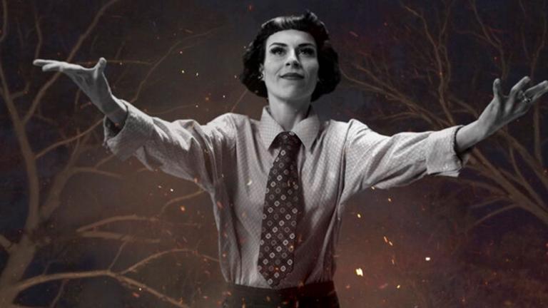 A young woman with short dark hair wearing a business shirt and tie with her arms stretched out wide in front of her. Behind her in the night sky there are tree branches, stars and flickering flames