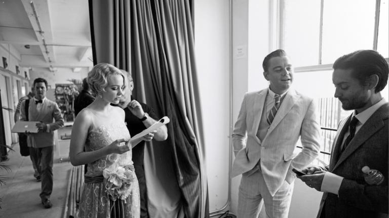 Actors Carey Mulligan, Leonardo DiCaprio and Tobey Maguire standing in a room in a semi-circle. They are on a film set dressed in 1920s costumes.