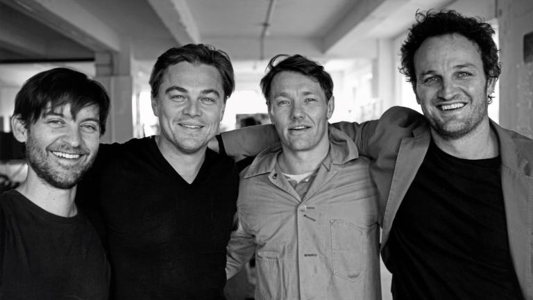Four men (actors Tobey Maguire, Leonardo DiCaprio, Joel Edgerton and Jason Clarke) standing side by side with their arms around each other and smiling directly at the camera.