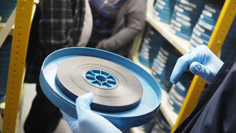 Close up of a person's gloved hands holding a canister with a reel of film in it.