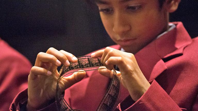 A young boy in a school uniform looking closely at a strip of film.