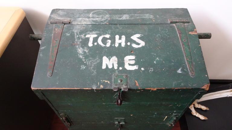 A large metal locked box with capital letters written on the top - T.G.H.S and underneath that - M.E.