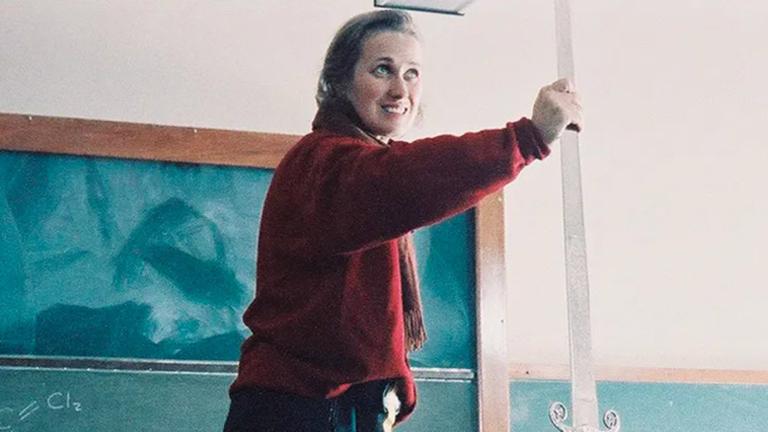 Director Jane Campion on the set of a film with her arm outstretched standing in front of a chalkboard in a classroom.