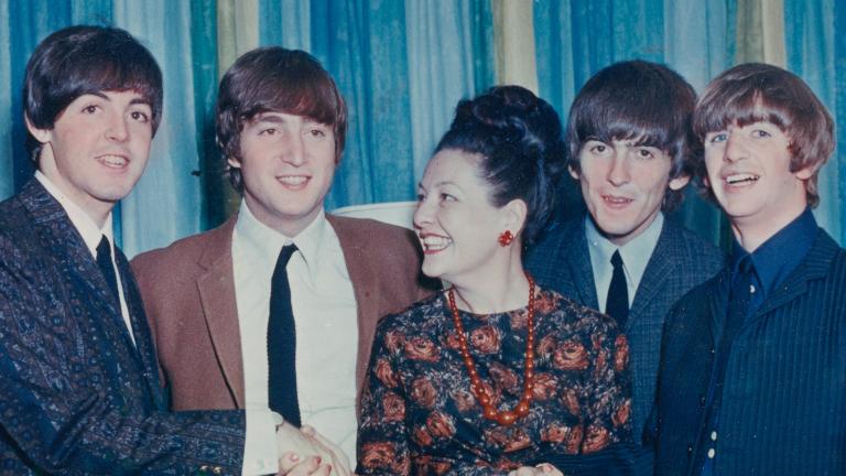 The Beatles band members standing side by side with radio personality Binny Lum in the centre. They are smiling and laughing together.
