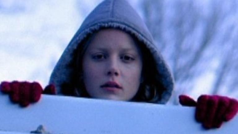 Scene from the film Somersault featuring actor Abbie Cornish outside in the snow wearing a hood and red gloves and peering over a fence.