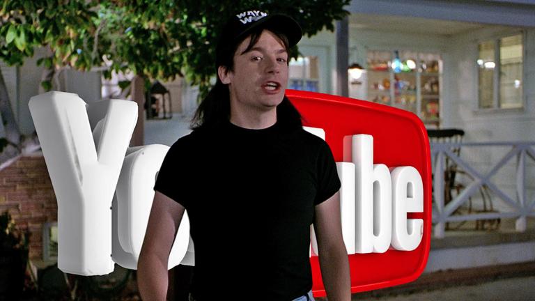 Mike Myers dressed as his character from the film Wayne's World pictured in front of a big YouTube sign.