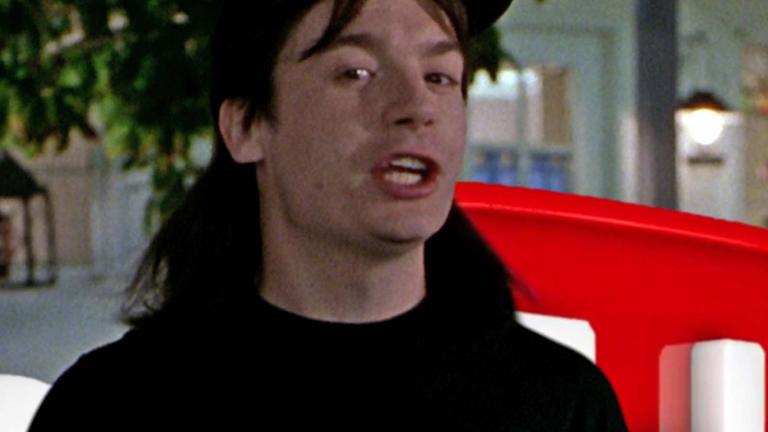 Mike Myers from Wayne's World standing in front of a partially obscured YouTube logo sign
