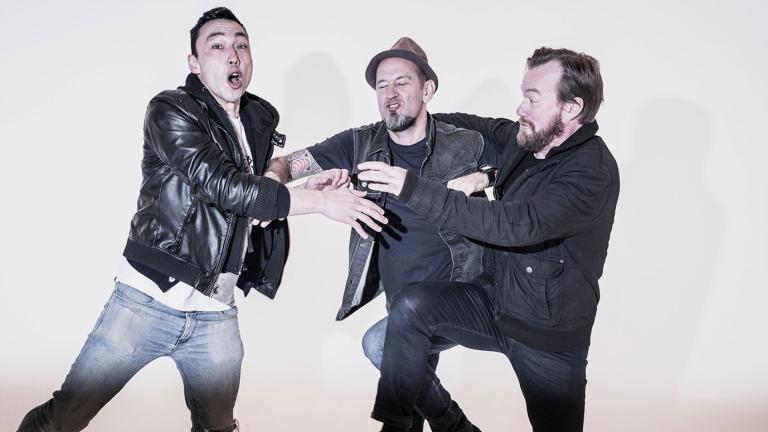 Three band members from Regurgitator comically pushing and shoving each other. 