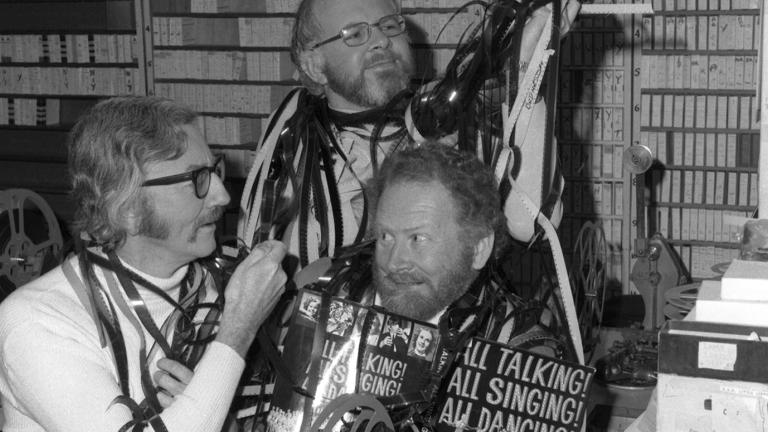 Ivan Hutchinson, Jim Murphy and Geoff Owen-Taylor in a studio, comically wrapping long strips of film around themselves. 