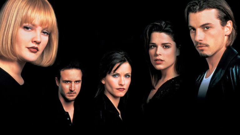 A production still from the film Scream showing a row of five men and women dressed in black and against a black background standing looking very serious, directly facing the camera 