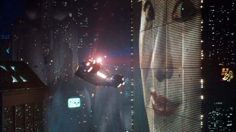 A helicopter hovers in a futuristic neon cityscape beside a giant advertising screen showing a smiling Japanese woman's face