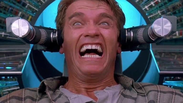 Close up of actor Arnold Schwarzenegger in a scene from the film Total Recall. He is attached to a machine and has an expression on his face that looks like he is in extreme pain.