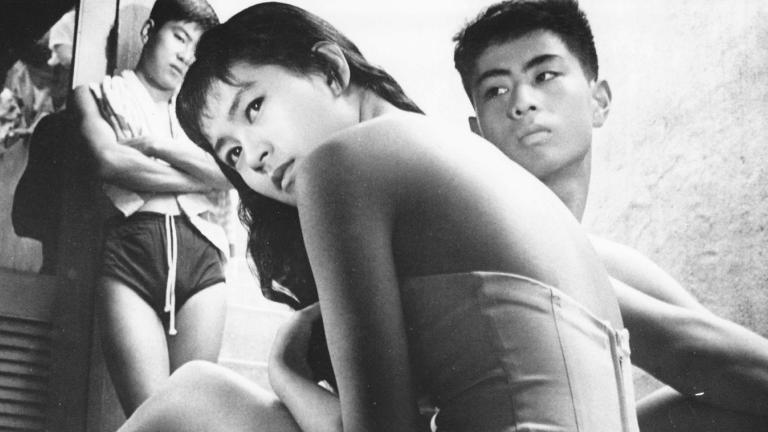 Three Japanese teenagers, two boys in the background and a girl looking back over her shoulder in the foreground.