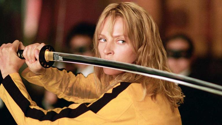 Close up of actor Uma Thurman holding a sword in both hands and wearing a yellow tracksuit with a black stripe in a scene from Kill Bill Volume 1.