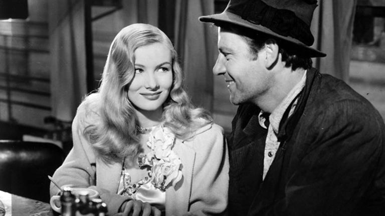 Actors Veronica Lake and Joel McCrea sitting next to each other in what appears to be a bar or a diner. They are smiling at each other and leaning in towards each other.