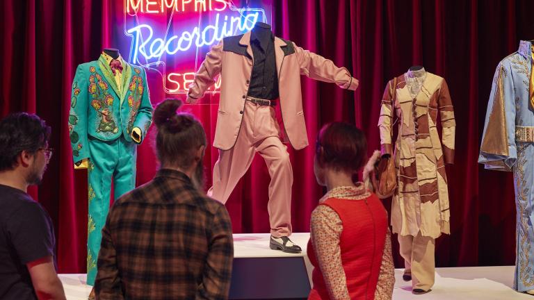 Three people viewing multiple costumes from the film ELVIS!