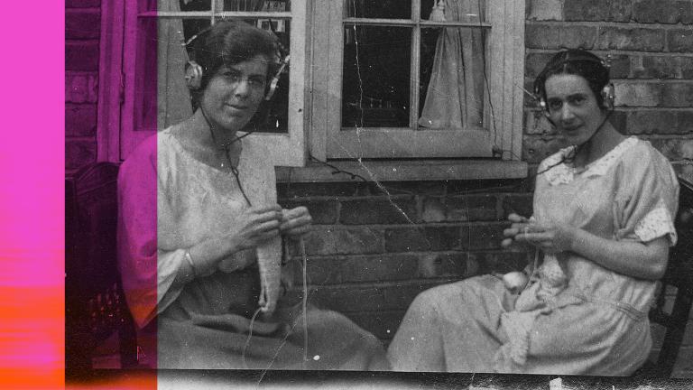 Two women sitting outside knitting and listening to the radio through headphones, c1920s