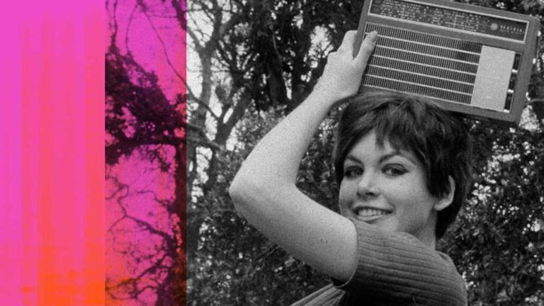 Close up of a young woman holding a portable radio on top of her head as she smiles at the camera.