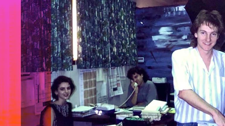 Announcer Richard Kingsmill in a community radio station in the 1980s. Two people are seated at a desk, one of them on the telephone
