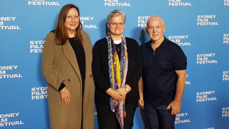 Two women and a man standing in front of a media wall.
