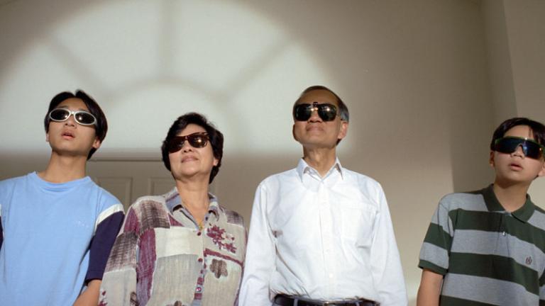 An Asian family all wearing sunglasses and staring out of a window.