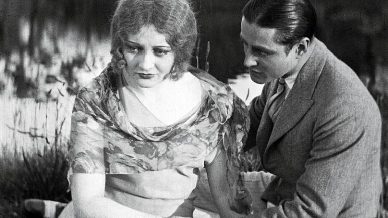 A young woman and man holding hands and looking forlorn in a scene from silent film The Cheaters.