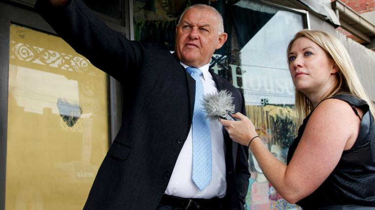 Policeman Ron Iddles with journalist Rachel Brown standing in front of a shop on a Melbourne street. 