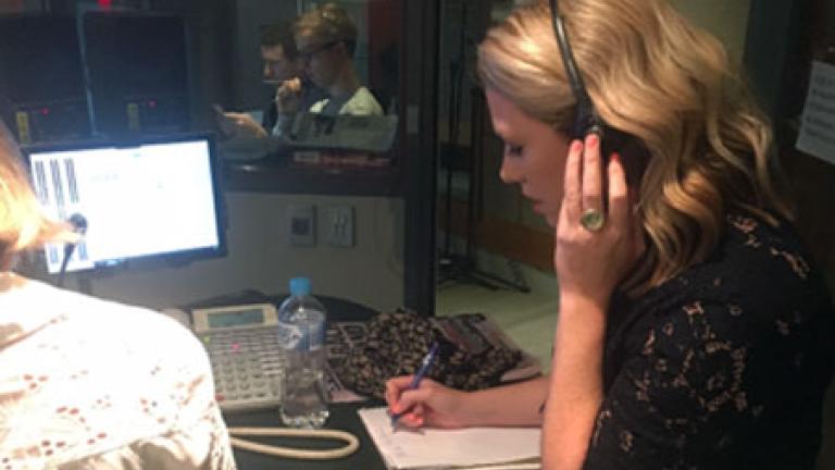 Journalist Rachael Brown with headphones on and writing on a notepad