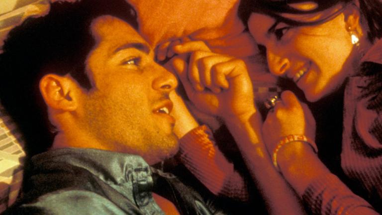A close up of a young man and woman lying on a bed, facing each other.