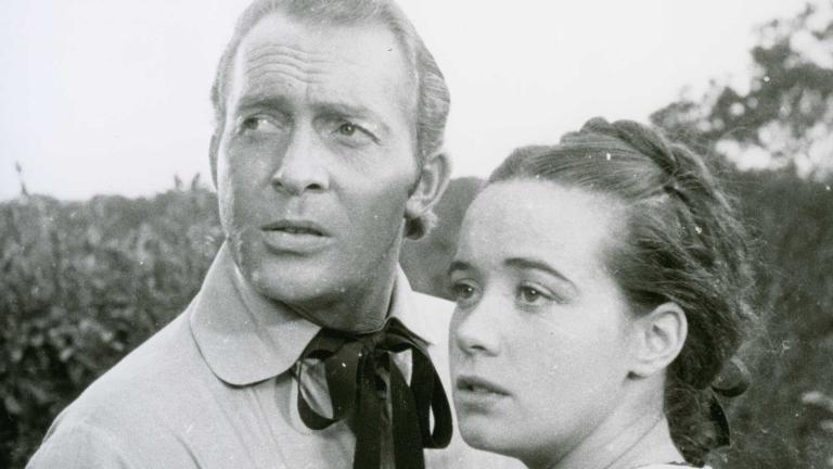 A man and woman standing close together outside while looking to the distance