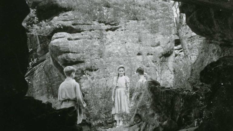 Three children standing in front of a cliff outside a cave