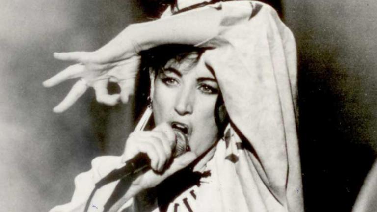 Image of singer Grace Knight performing on stage. She is singing into a microphone and kicking her leg up in the air.