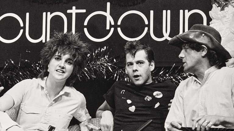 A woman and two men sitting on a couch under a sign that says 'countdown'