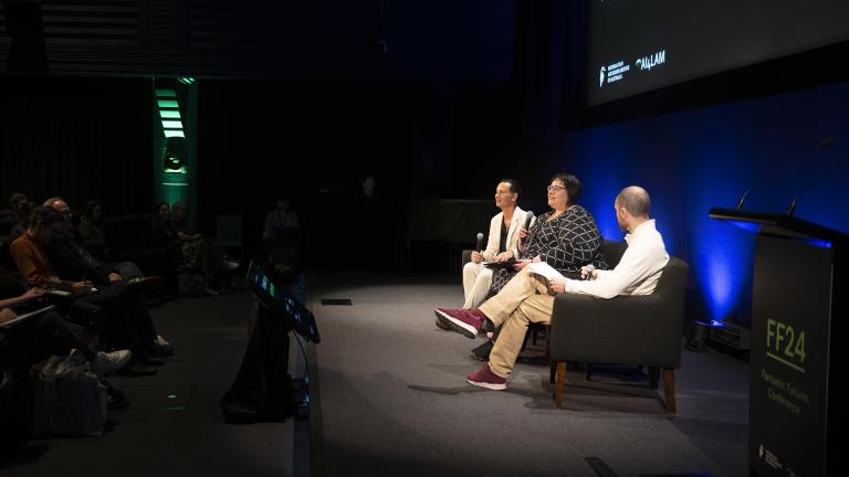 Peter-Lucas Jones, Kathy Reid and Keir Winesmith presenting a panel on a stage