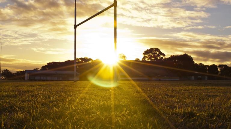 The rugby league goal posts on a football pitch are backlit by the setting sun