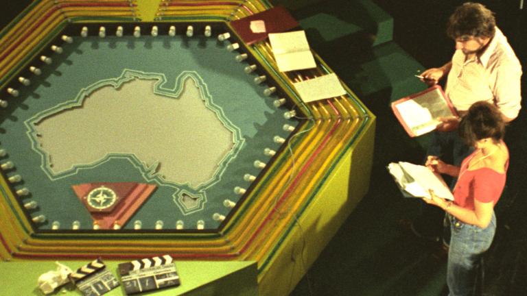 Elevated view of a TV game show's crew members on set next to a prop with a map of Australia