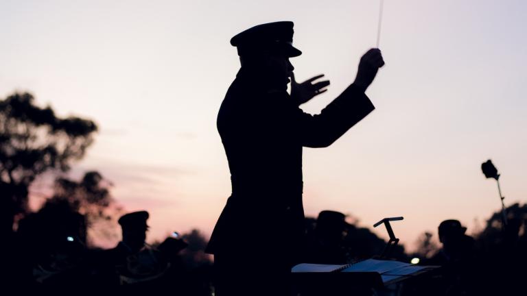 A silhouette of an orchestra conductor in military uniform waving his baton during a dawn service on Anzac Day