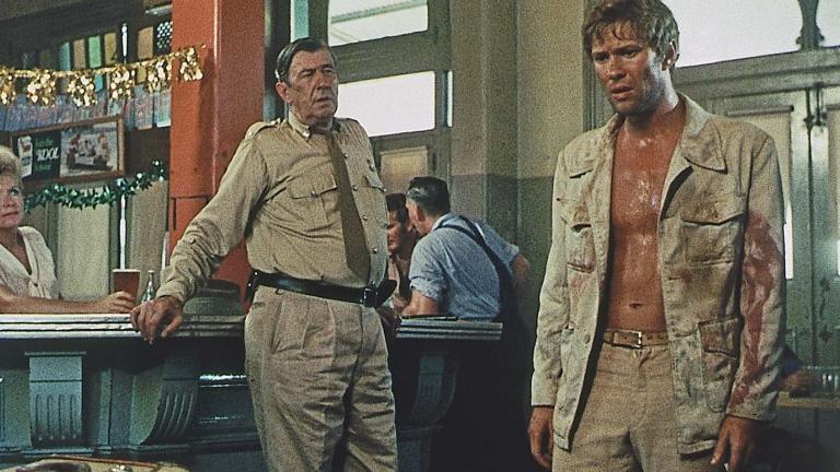 An outback police officer appraises a sweaty dishevelled looking man who has entered a pub in a scene from the 1971 film Wake in Fright