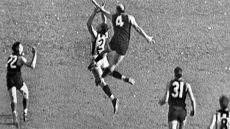Two Australian Rules players jump for the ball while others look on in the 1964 VFL Grand Final