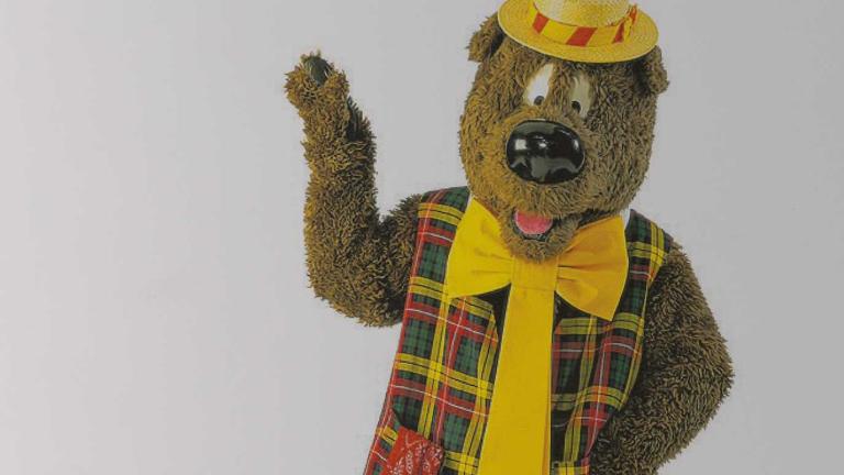 Upper body image of children's TV character Humphrey B. Bear wearing a plaid vest, yellow tie and boater hat.