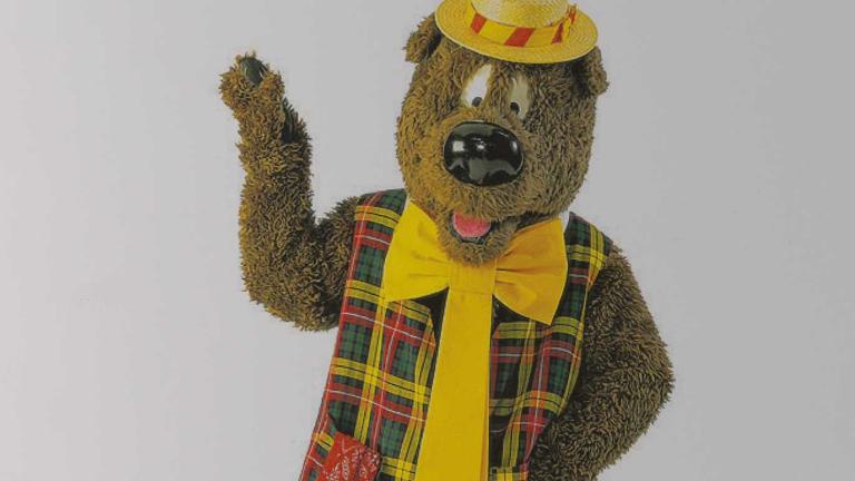 Upper body image of children's TV character Humphrey B. Bear wearing a plaid vest, yellow tie and boater hat.