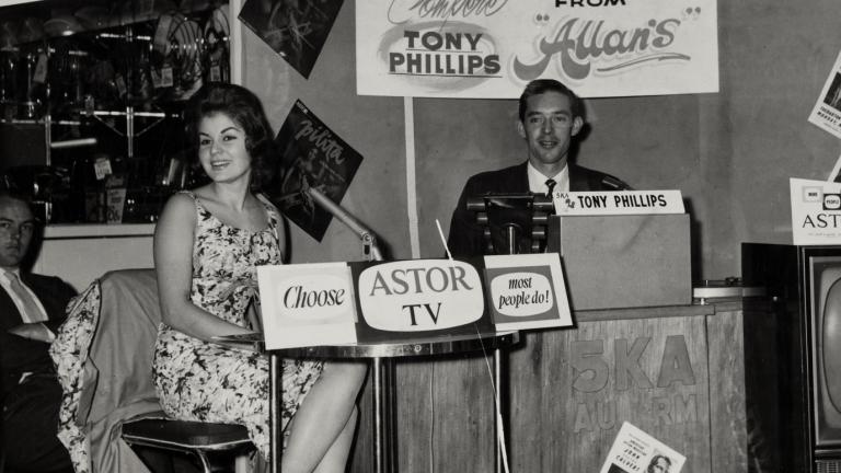 Pilita Corrales seated behind a desk at an outdoor broadcast with radio station 5KA DJ Tony Phillips. NExt to the desk is an Astor TV set