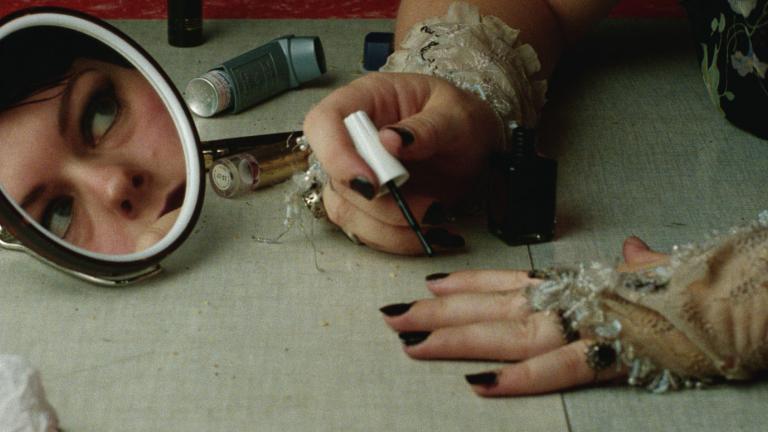 Genevieve Lemon's face is reflected in a small mirror while she applies black fingernail polish.
